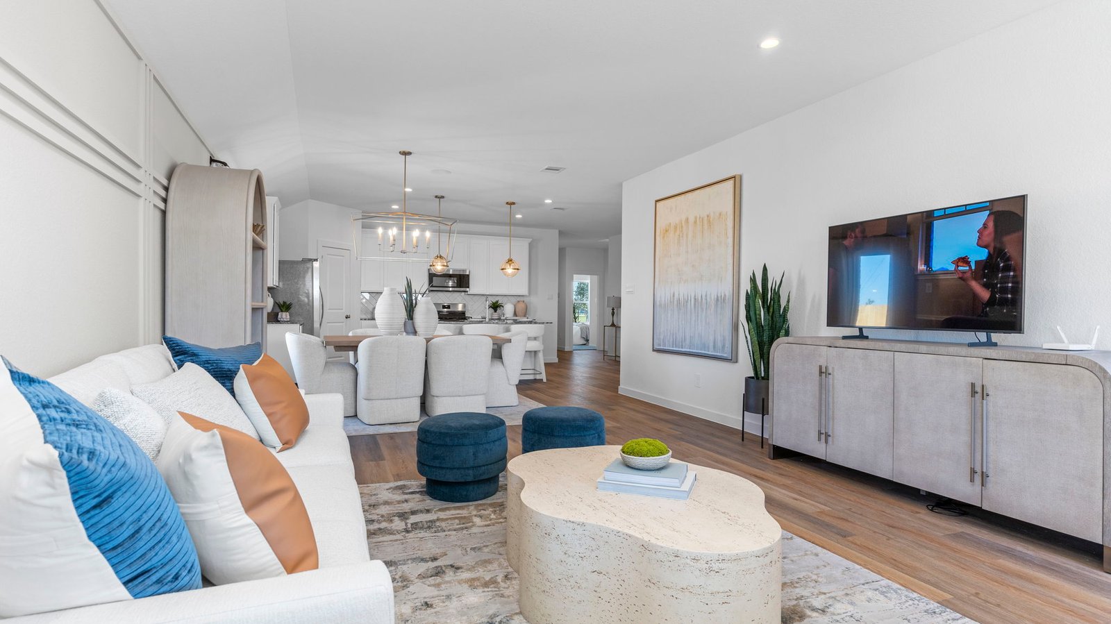 A cozy living room featuring large windows for natural lighting, wood flooring and a view to the kitchen and dining area.