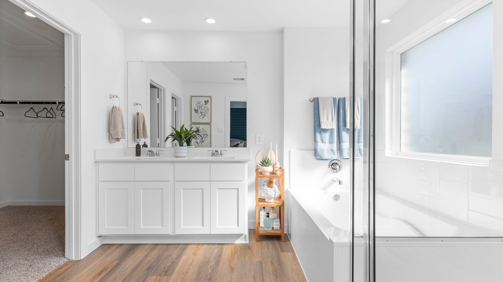 Modern primary bathroom with double vanities, quartz countertops, and a glass-enclosed shower with a walk-in closet.