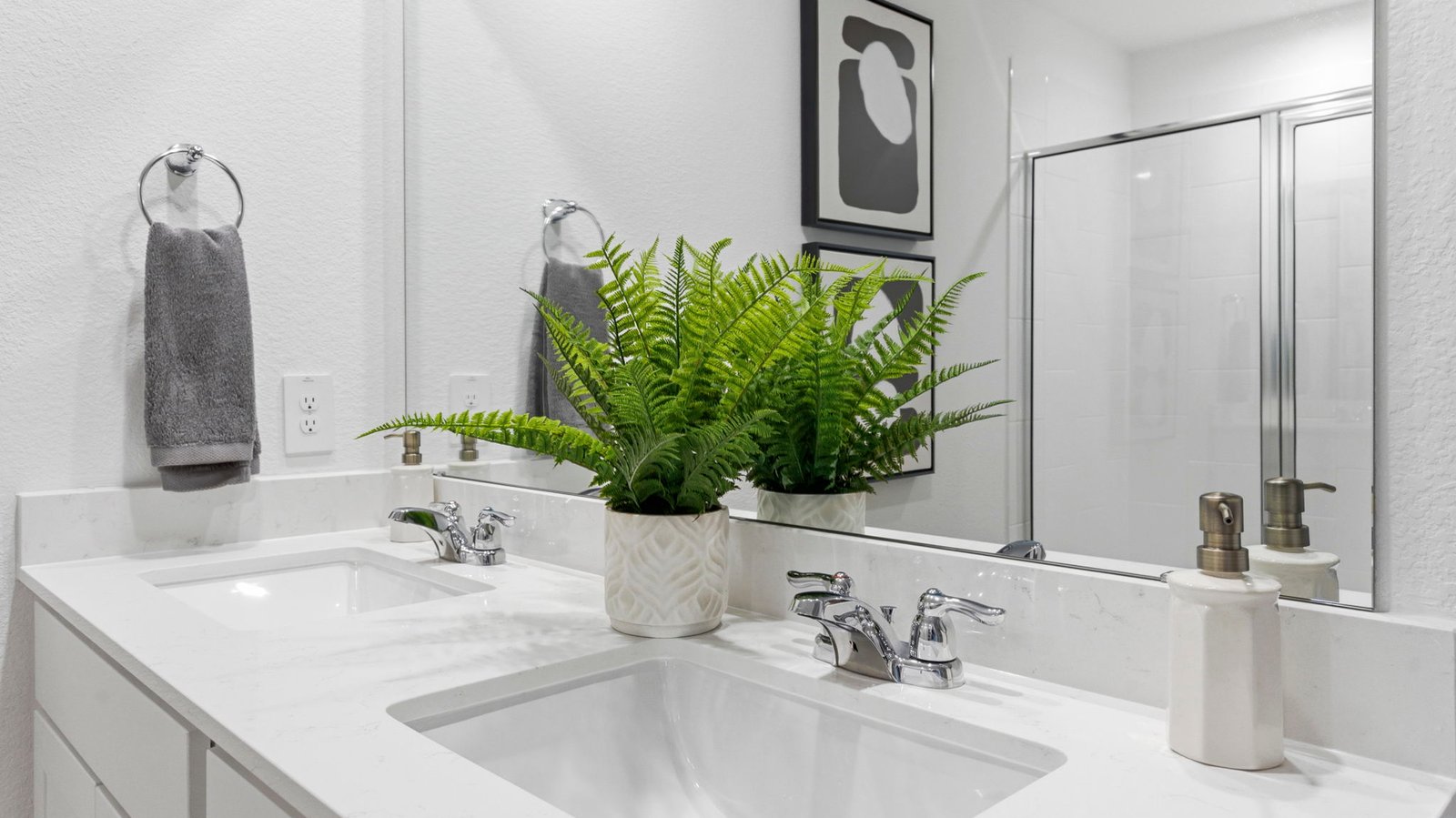Modern primary bathroom with double vanities, quartz countertops, and a glass-enclosed shower with a walk-in closet.