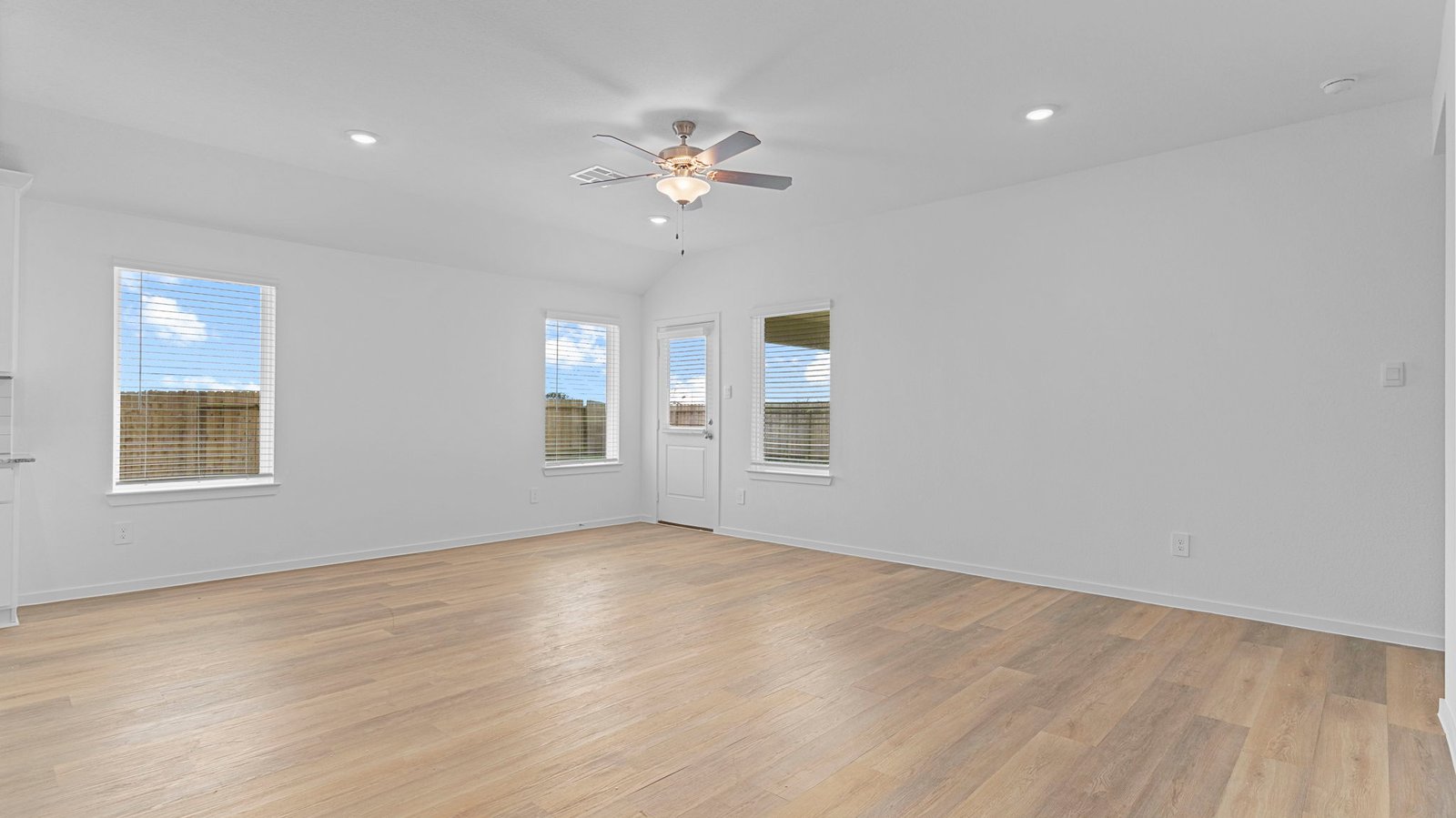 A cozy living room featuring large windows for natural lighting, wood flooring and a view to the kitchen and dining area.