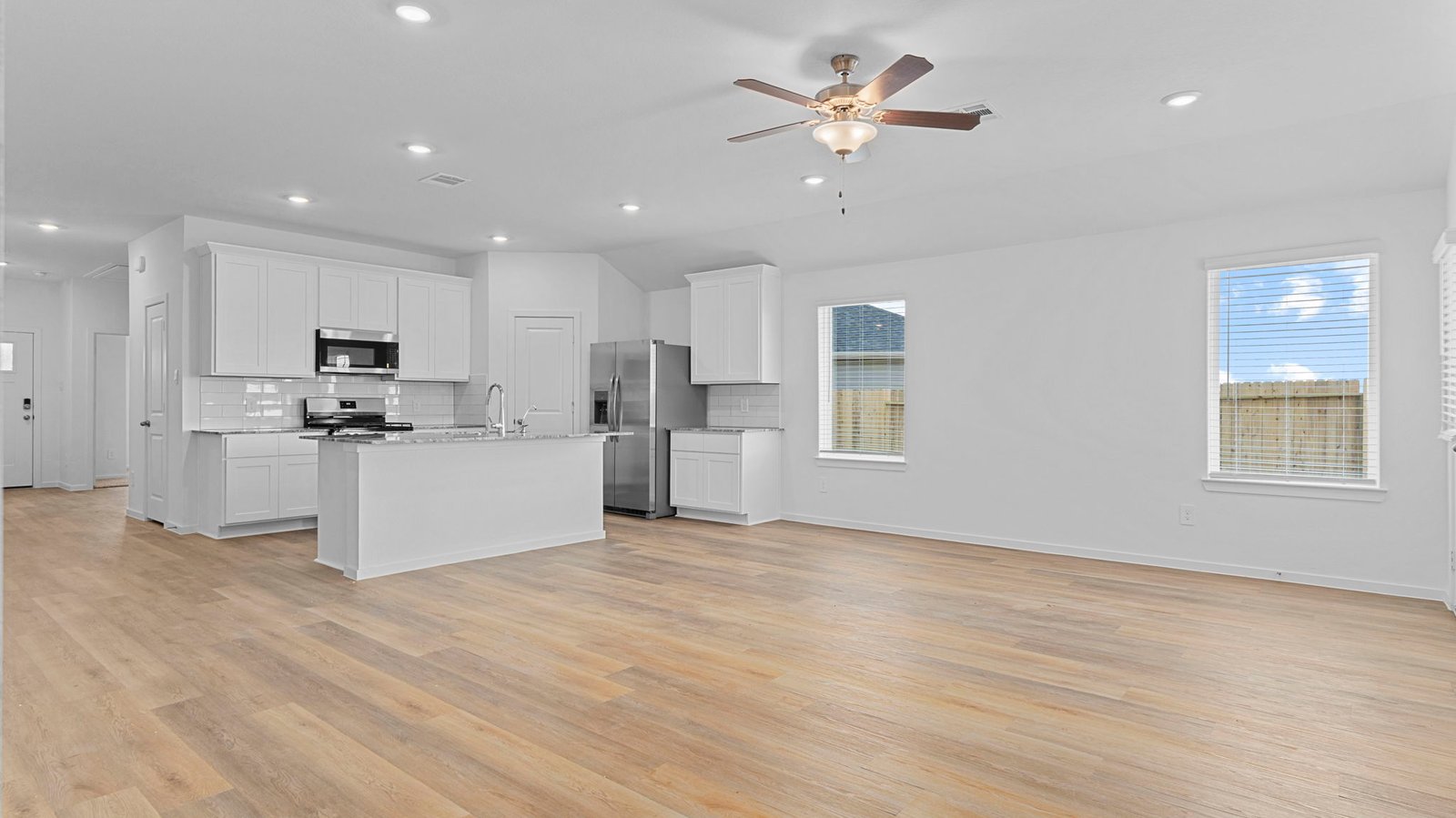 A cozy living room featuring large windows for natural lighting, wood flooring and a view to the kitchen and dining area.