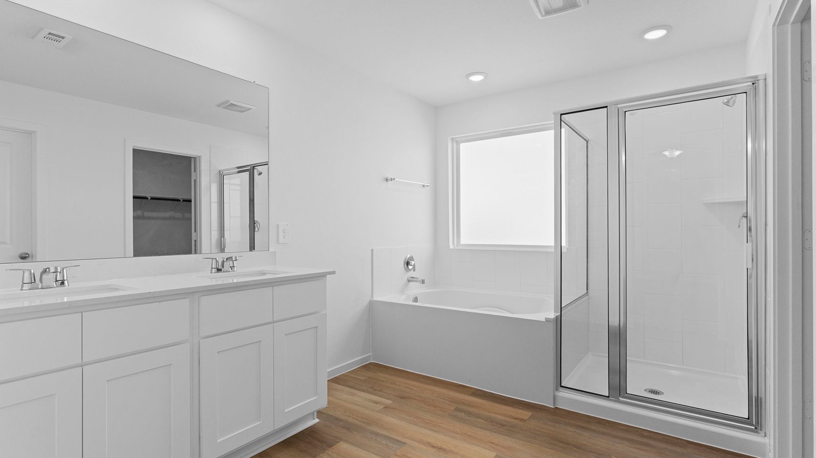 Modern primary bathroom with double vanities, quartz countertops, and a glass-enclosed shower with a walk-in closet.