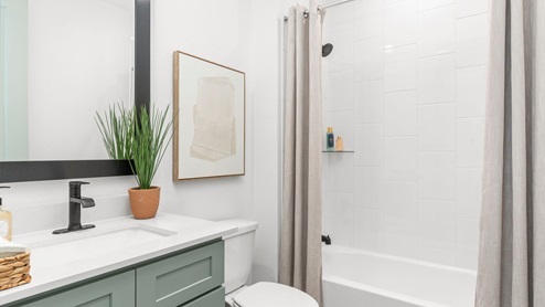 Bathroom with single sink pale green vanity and white granite tops with white tile shower and tub combo.