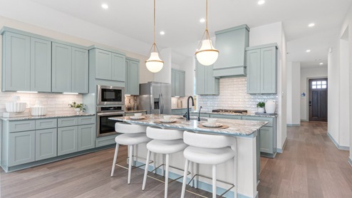 Kitchen area with light gray granite countertops, large island, pale green cabinets, white tile backsplash, and stainless steel appliances with pantry around the corner in the coffee nook.