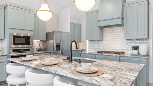 Large kitchen island with light gray granite top with kitchen cabiinets in the back.