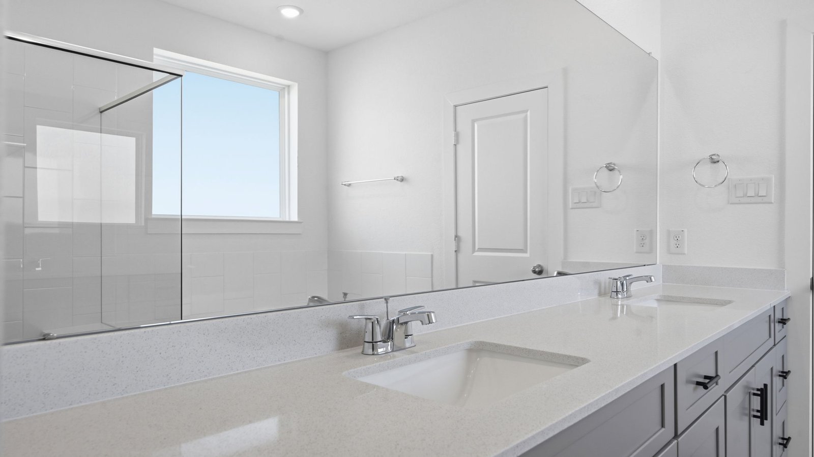 Modern primary bathroom with double vanities, quartz countertops, and a glass-enclosed shower with a walk-in closet.