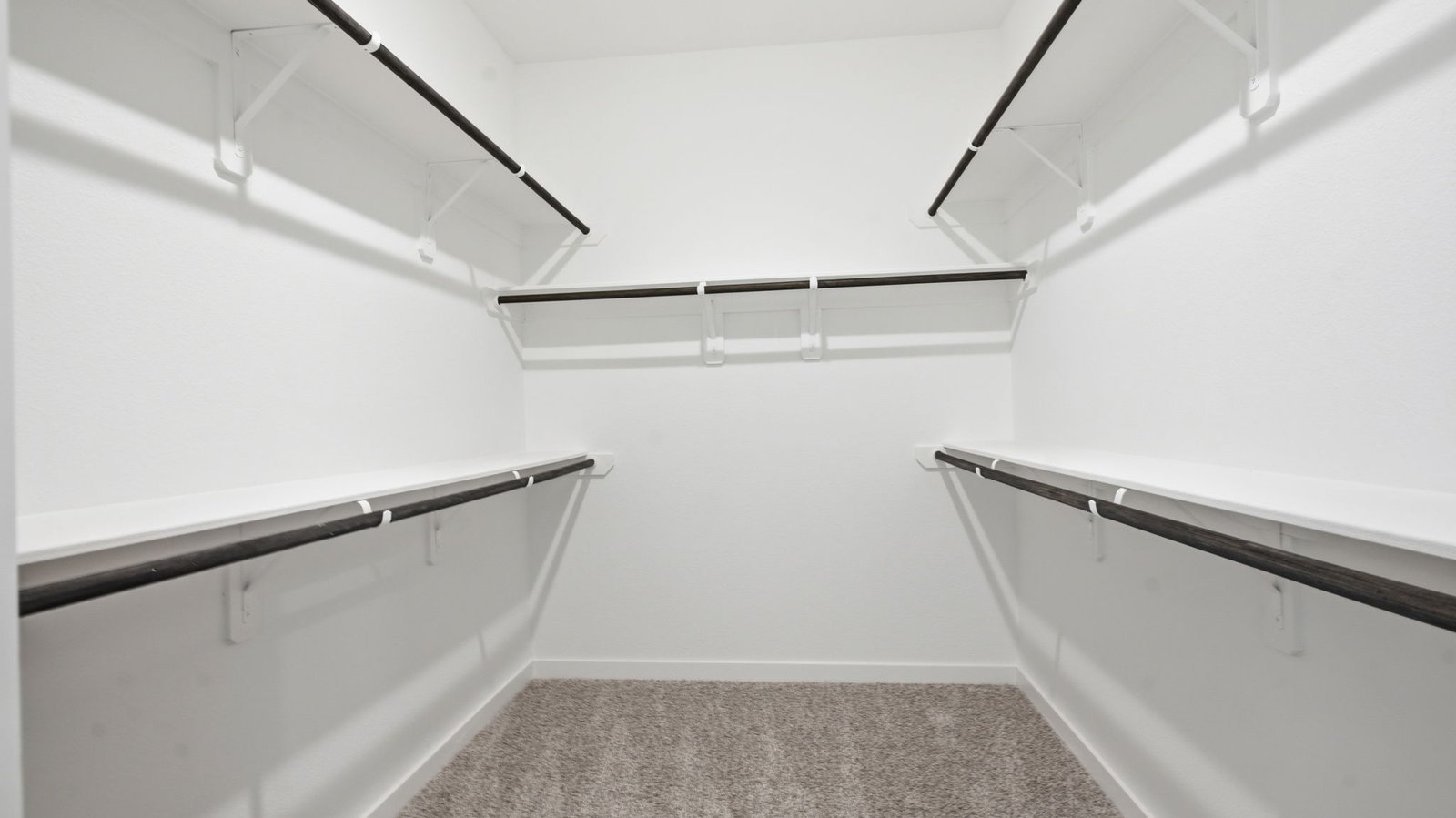 A spacious walk-in closet off the primary bathroom with multiple hanging rods, and shelves for maximum storage capabilities.