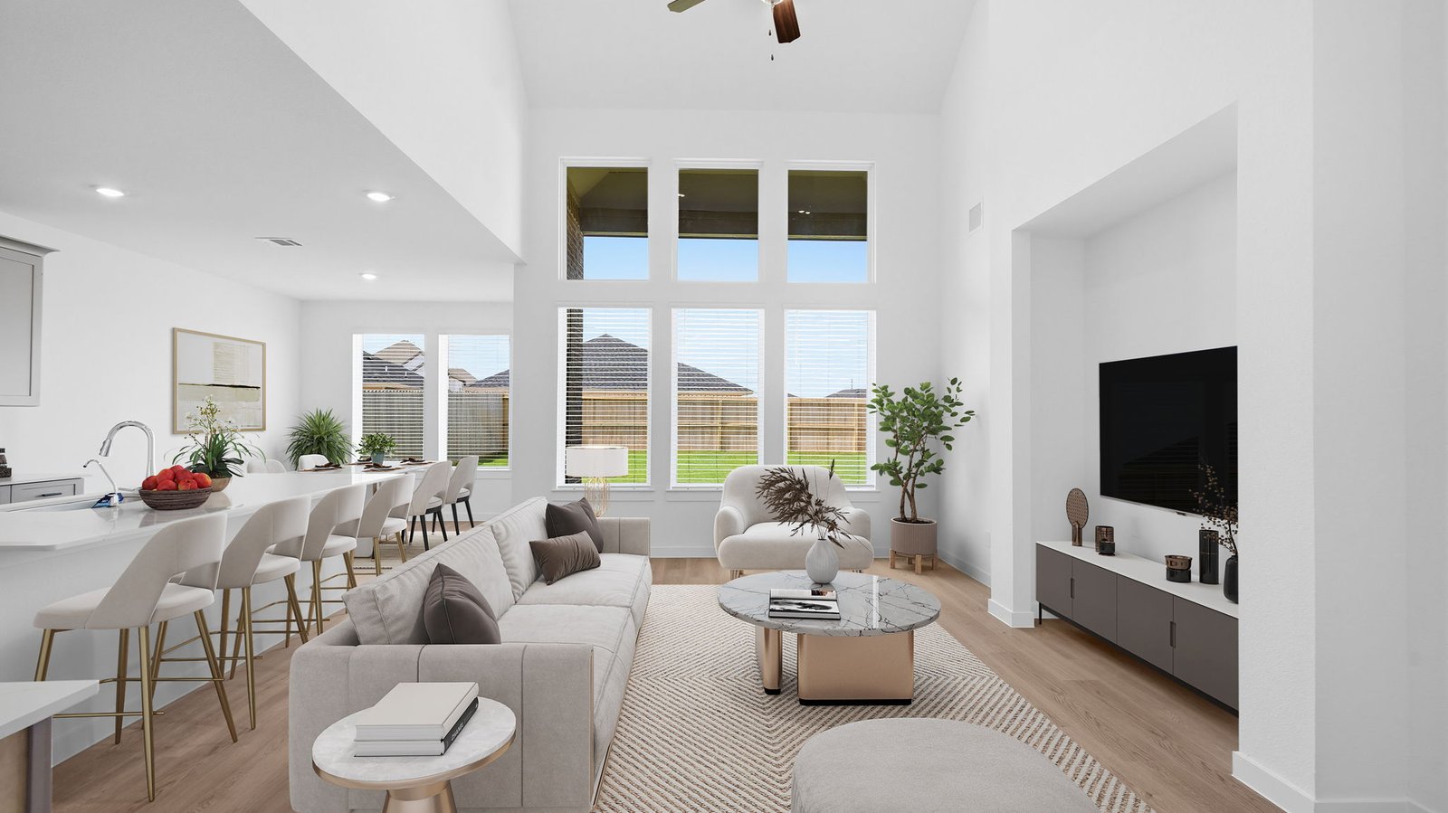A luxurious living room featuring tall ceilings, large windows for natural lighting wood flooring and a view to the backyard.