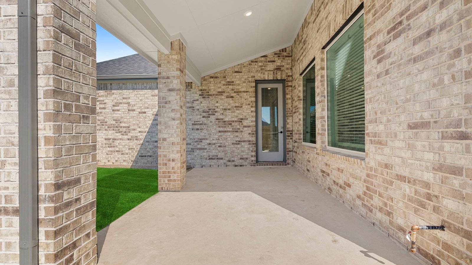 Outdoor covered patio with seating area overlooking a well-maintained lawn, perfect for relaxation.