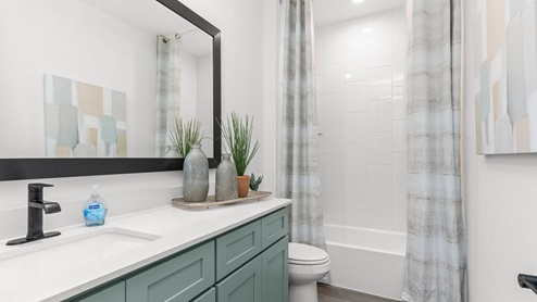 Second bathroom with single sink pale green vanity and white granite tops with white tile shower and tub combo.