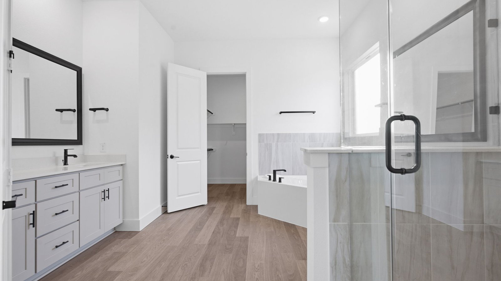 Luxurious primary bathroom with dual vanities, a soaking tub, glass-enclosed shower and walk-in closet.