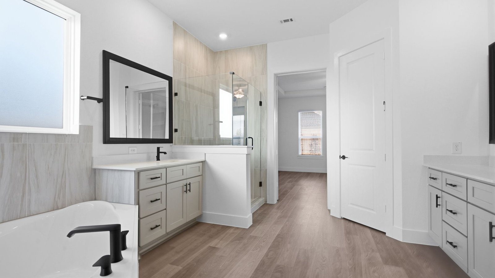 Luxurious primary bathroom with dual vanities, a soaking tub, glass-enclosed shower and walk-in closet.
