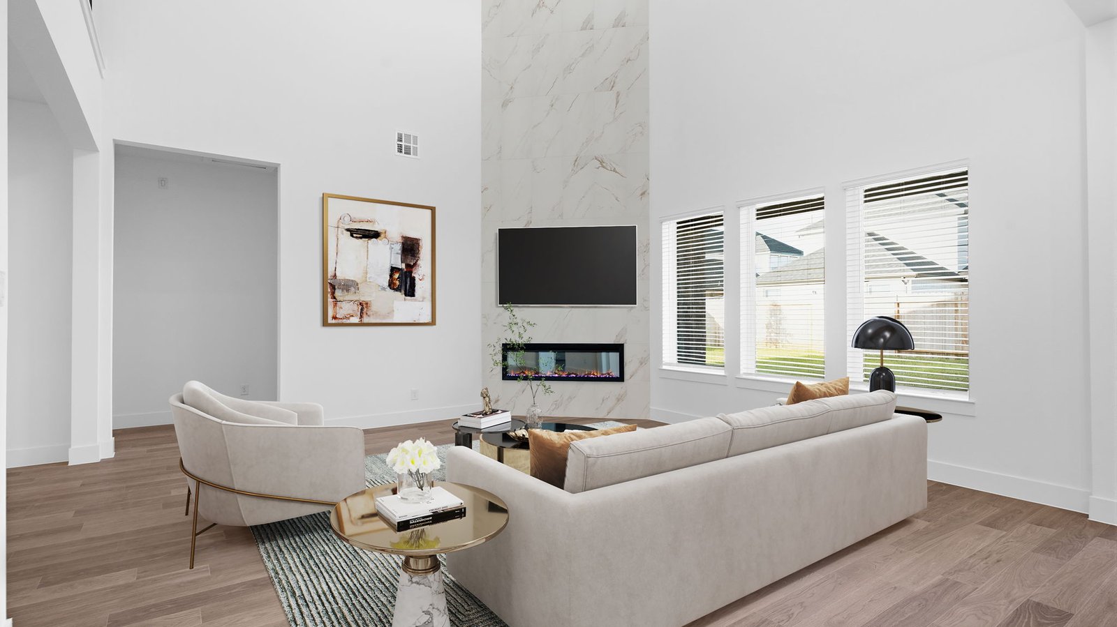 A luxurious living room featuring tall ceilings, large windows for natural lighting wood flooring and a view to the backyard.