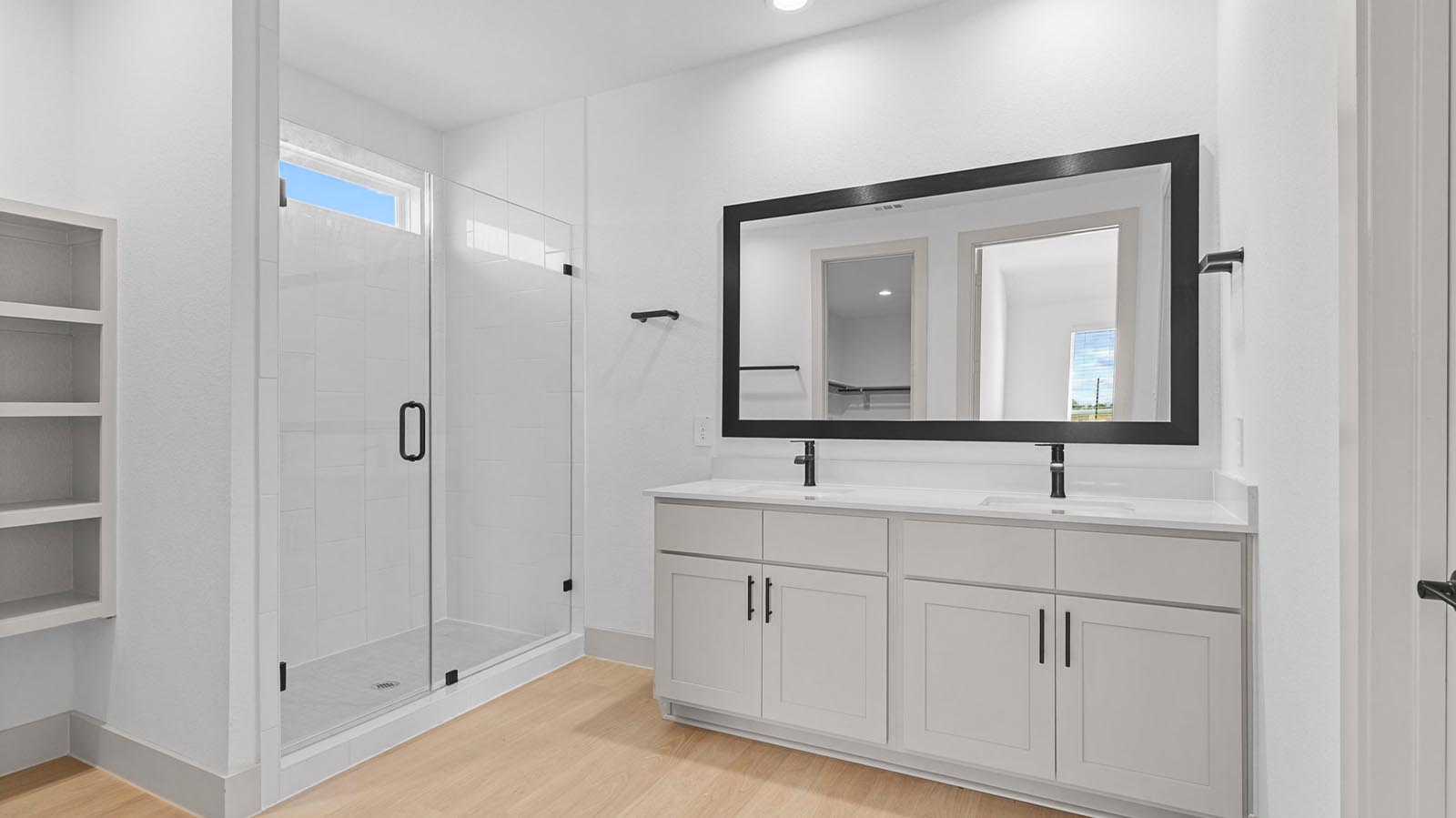 Modern primary bathroom with double vanities, quartz countertops, and a glass-enclosed shower with a walk-in closet.