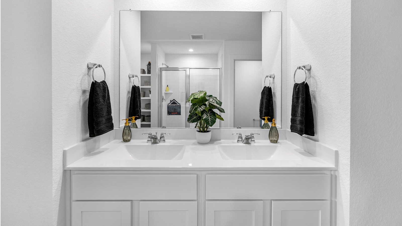 Modern primary bathroom with double vanities, quartz countertops, and a glass-enclosed shower with a walk-in closet.