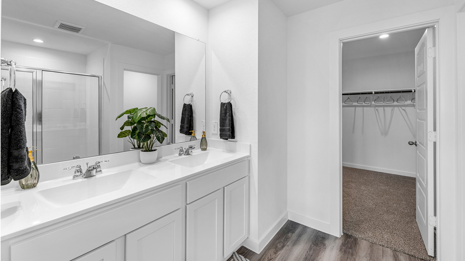 Modern primary bathroom with double vanities, quartz countertops, and a glass-enclosed shower with a walk-in closet.