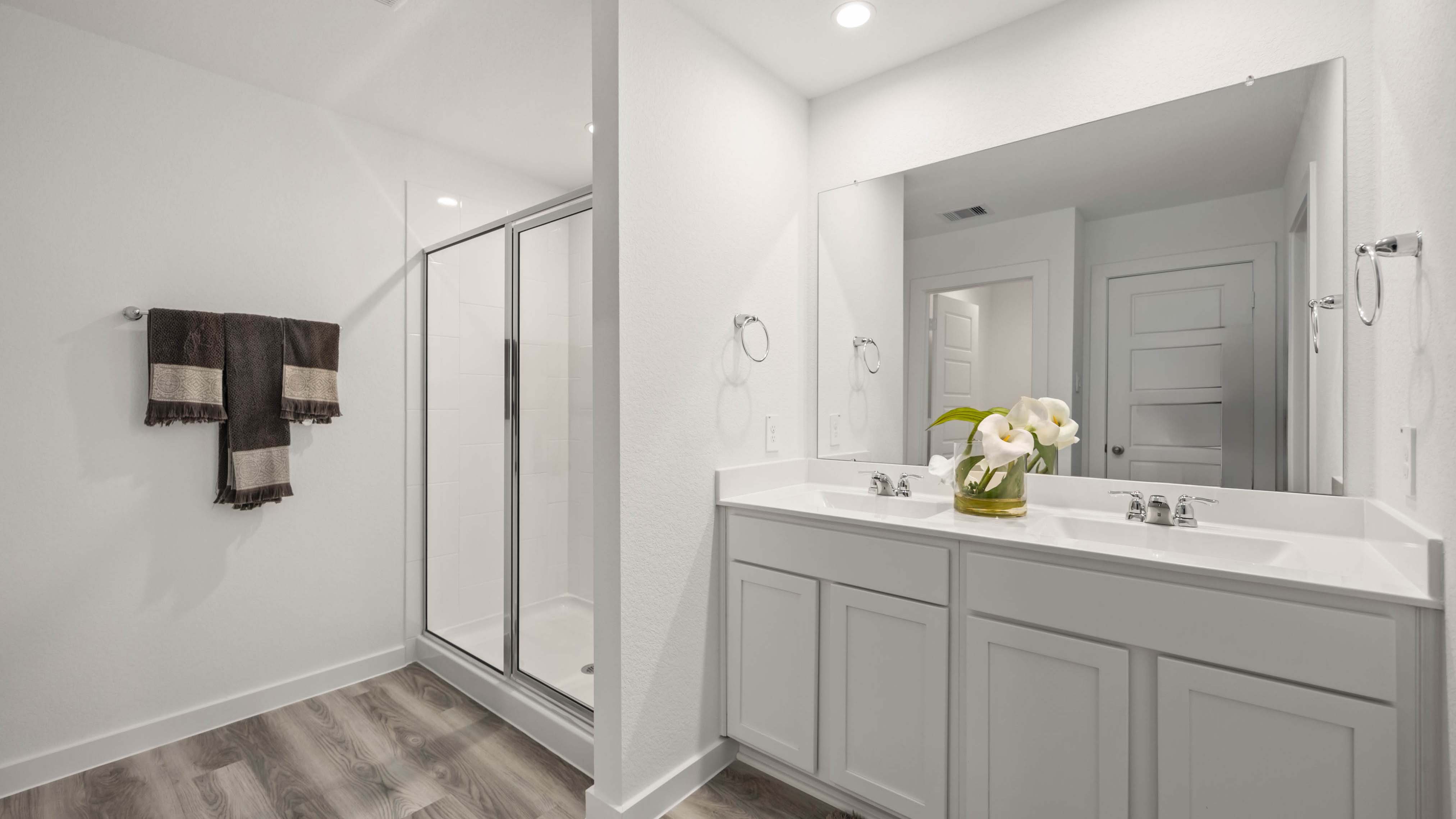 Modern primary bathroom with double vanities, quartz countertops, and a glass-enclosed shower with a walk-in closet.