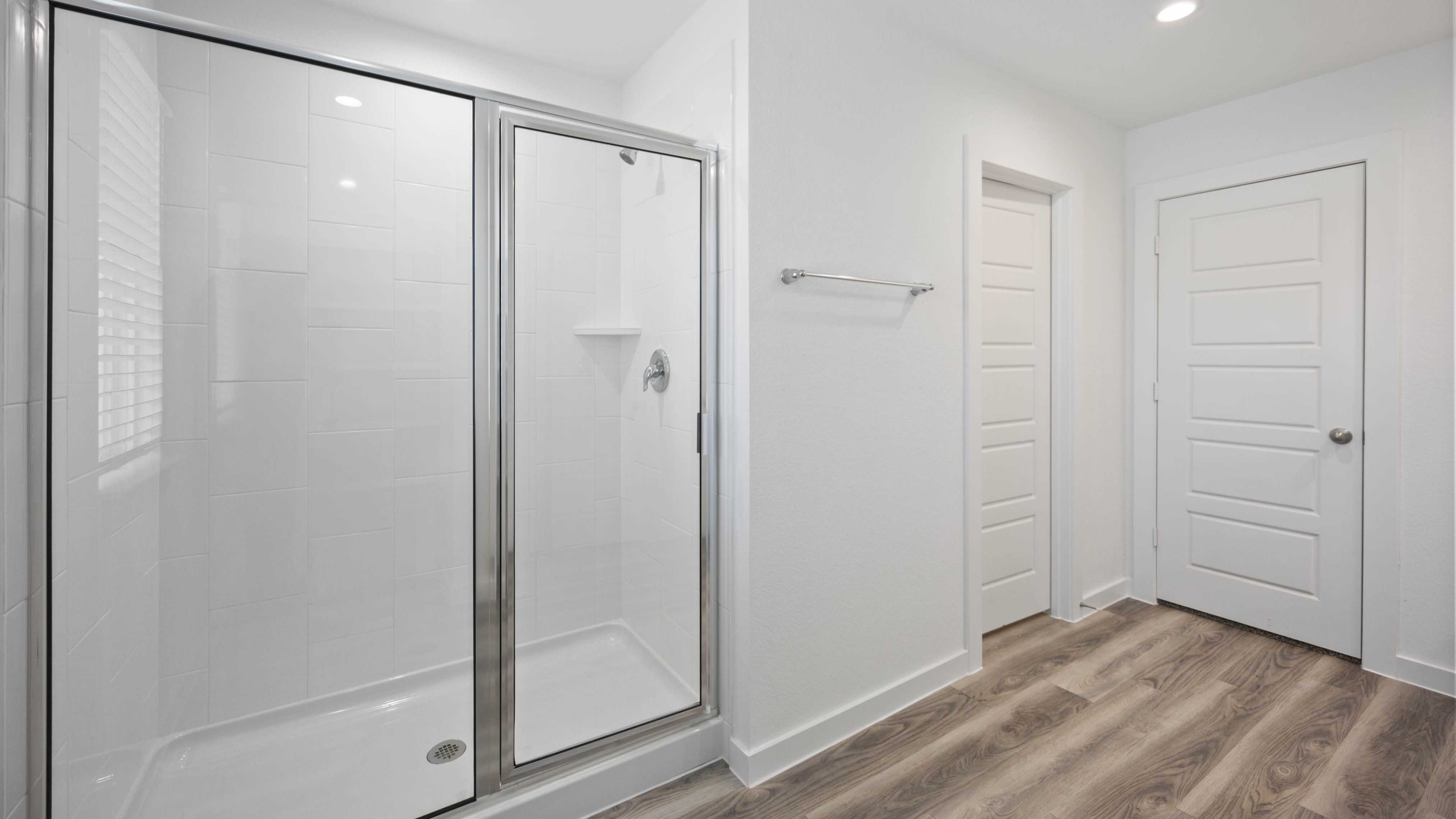 Modern primary bathroom with double vanities, quartz countertops, and a glass-enclosed shower with a walk-in closet.