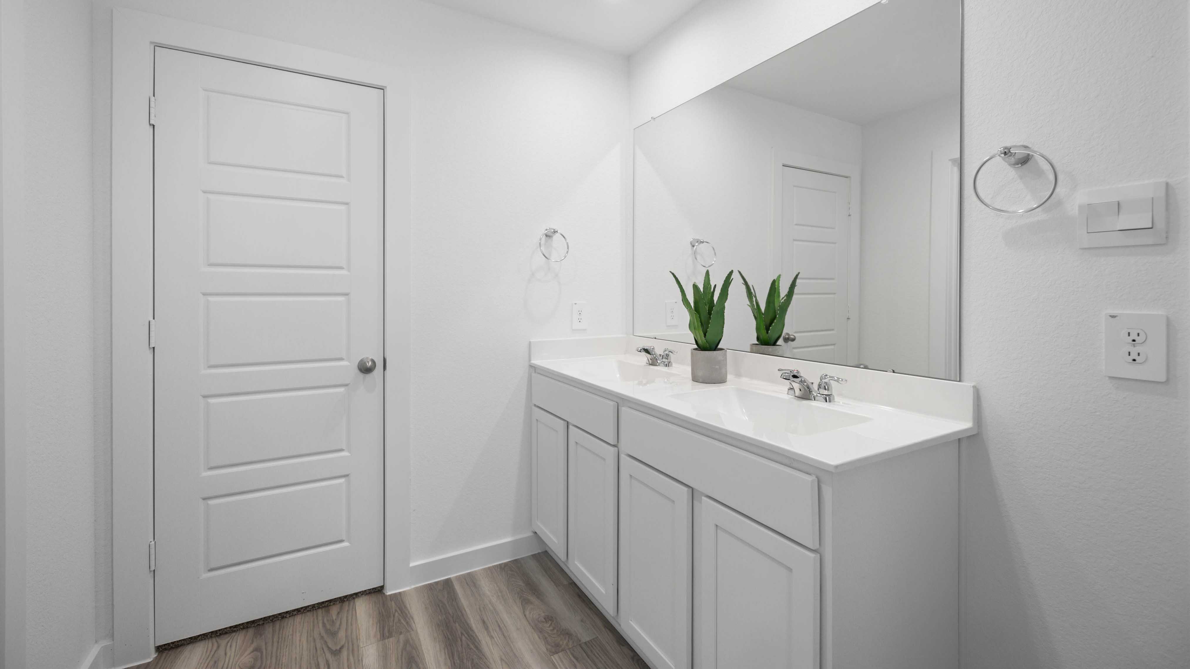 Modern primary bathroom with double vanities, quartz countertops, and a glass-enclosed shower with a walk-in closet.