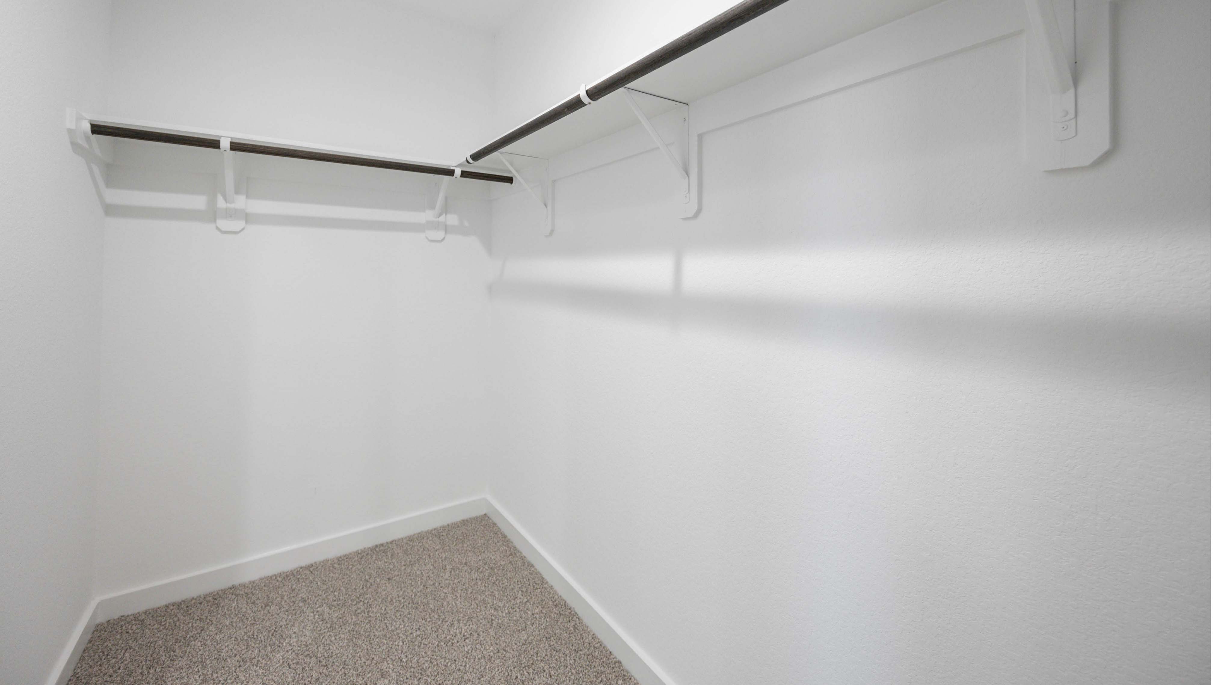 A spacious walk-in closet off the primary bathroom with multiple hanging rods, and shelves for maximum storage capabilities.