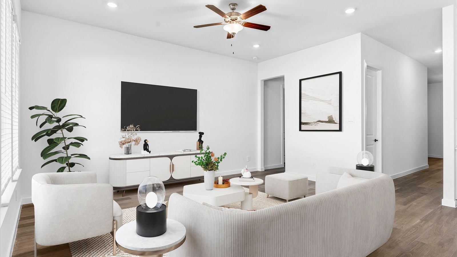 A cozy living room featuring large windows for natural lighting, vinyl wood flooring and a view to the kitchen and dining area.