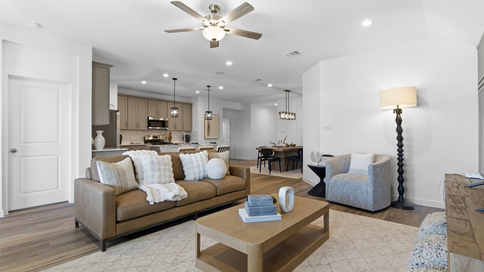 A cozy living room featuring large windows for natural lighting, vinyl wood flooring and a view to the kitchen and dining area.