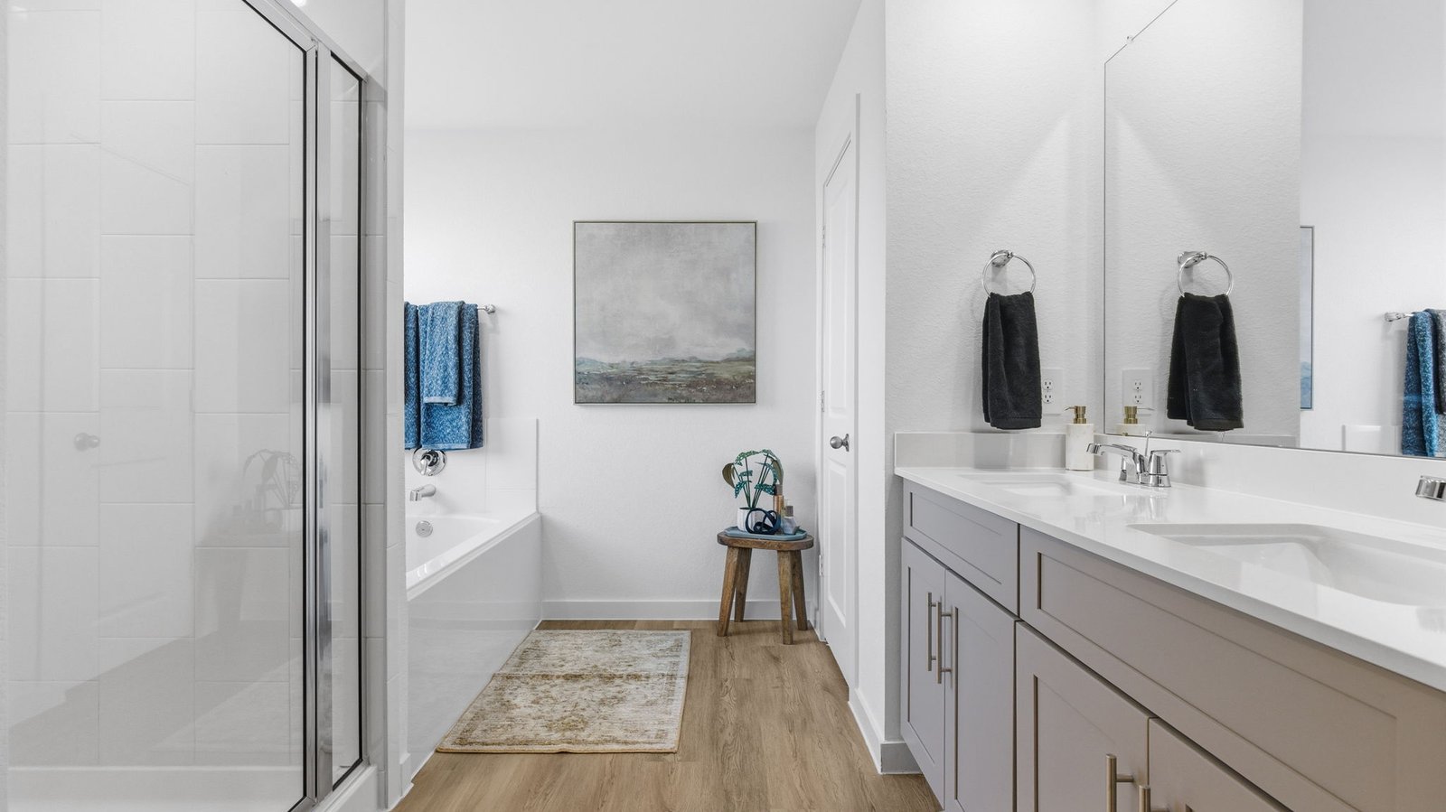 Modern primary bathroom with double vanities, quartz countertops, and a glass-enclosed shower with a walk-in closet.