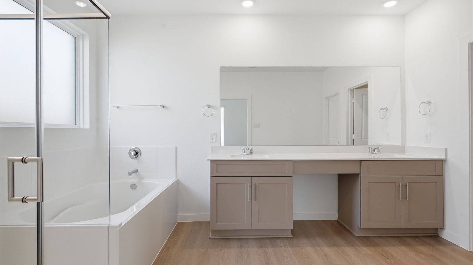 Modern primary bathroom with double vanities, and a glass-enclosed shower with a walk-in closet.