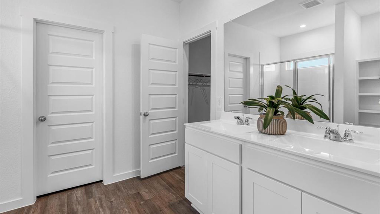 Modern primary bathroom with double vanities, granite countertops, and a glass-enclosed shower with a walk-in closet.