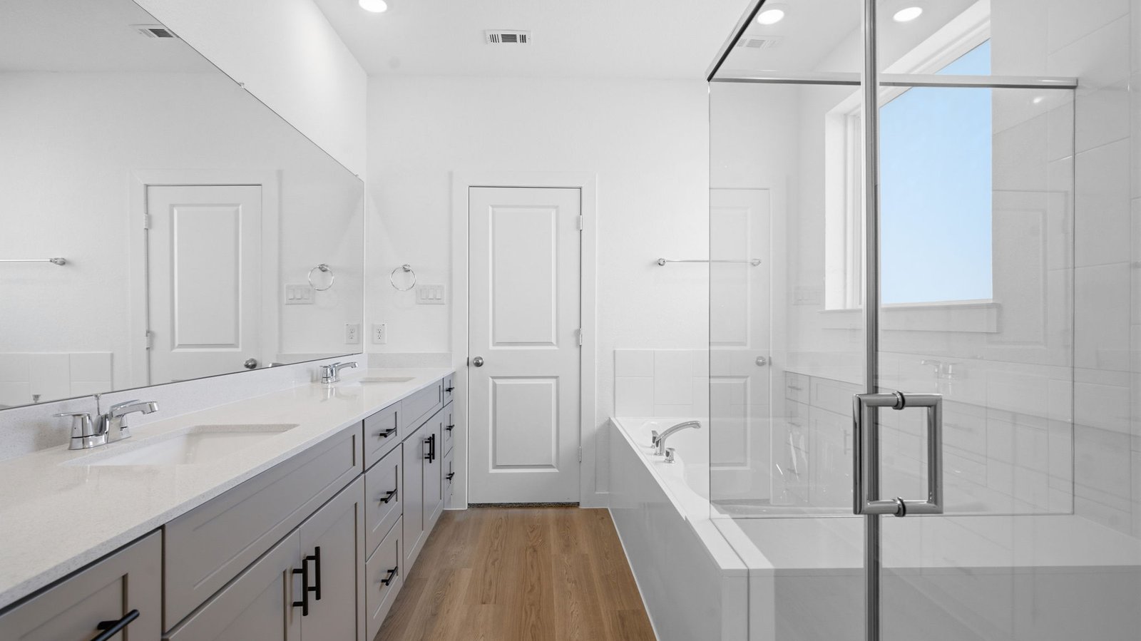 Modern primary bathroom with double vanities, quartz countertops, and a glass-enclosed shower with a walk-in closet.
