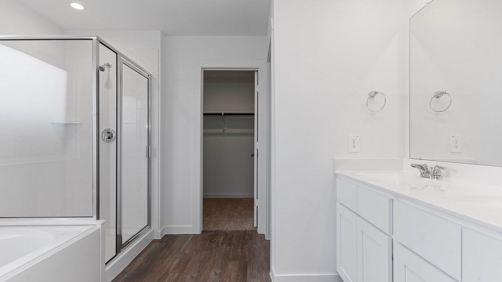 Modern primary bathroom with double vanities, granite countertops, and a glass-enclosed shower with a walk-in closet.