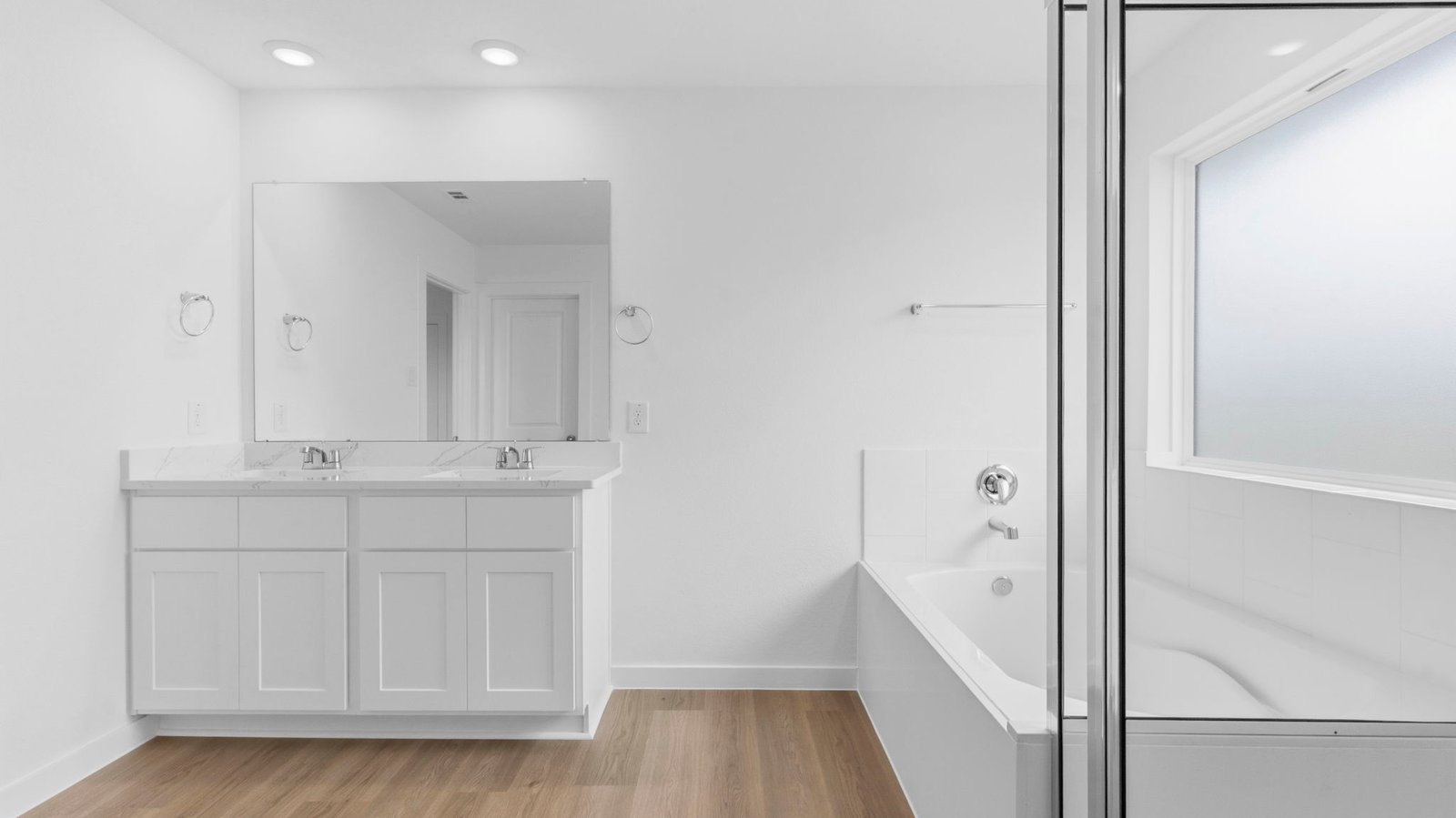 Modern primary bathroom with double vanities, quartz countertops, and a glass-enclosed shower with a walk-in closet.