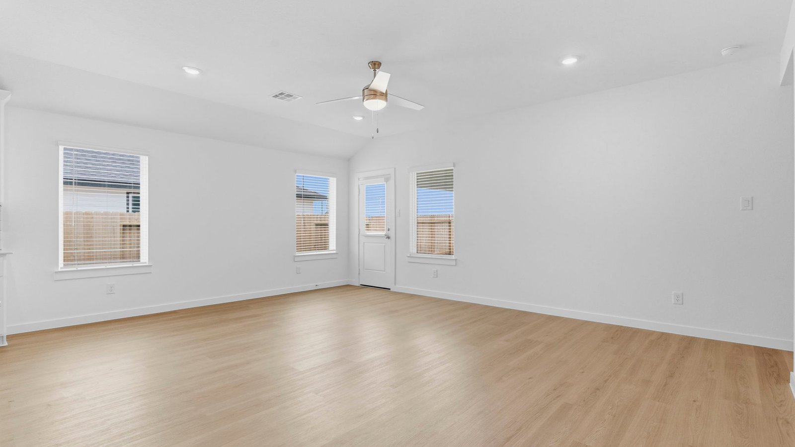 A cozy living room featuring large windows for natural lighting, vinyl wood flooring and a view to the kitchen and dining area.