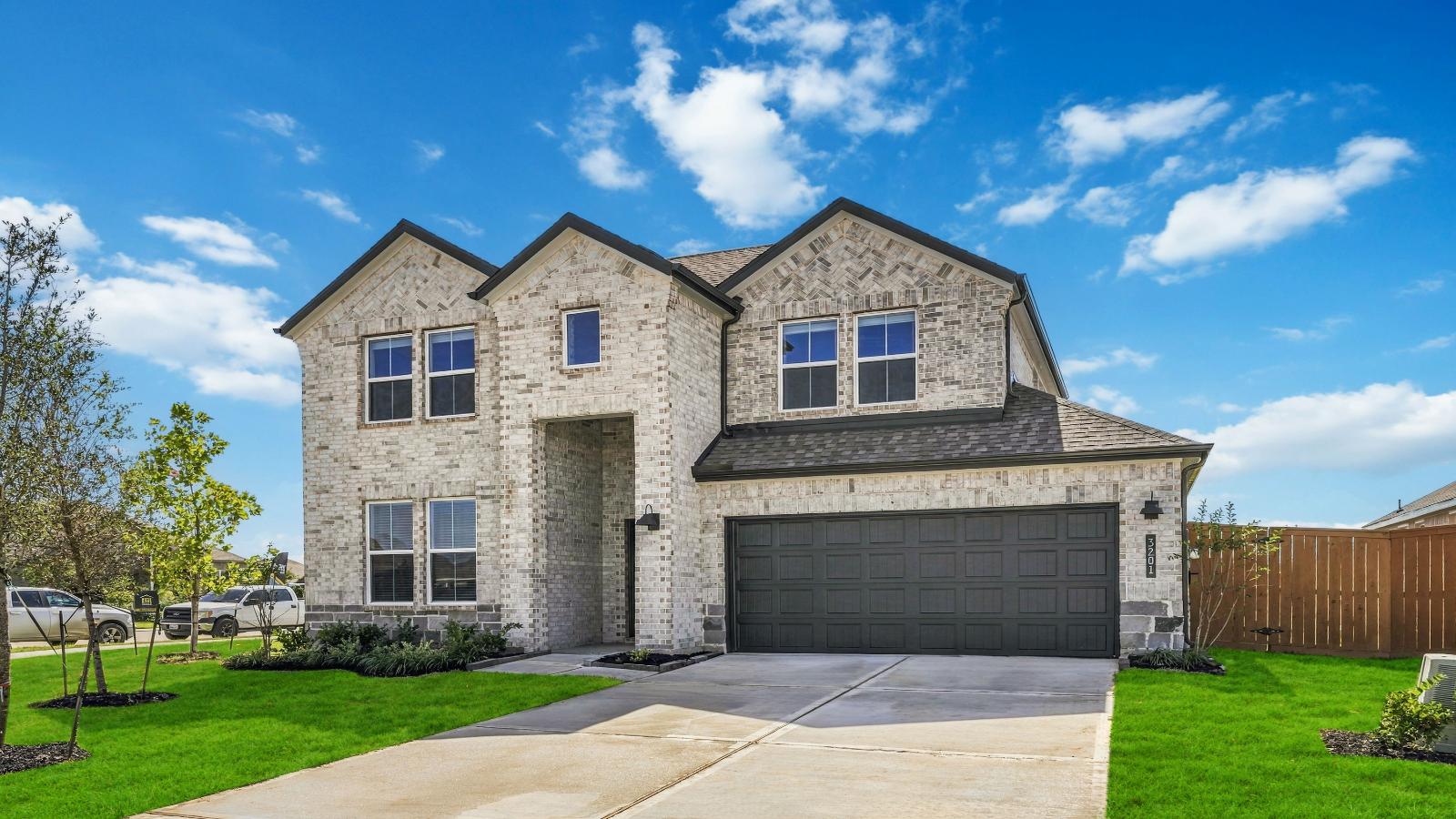 A two-story home with brick and stone exterior with a two-car garage and a well-maintained front lawn in Texas City
