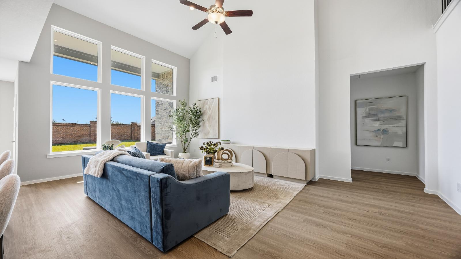 A luxurious living room featuring tall ceilings, large windows for natural lighting wood flooring and a view to the backyard.