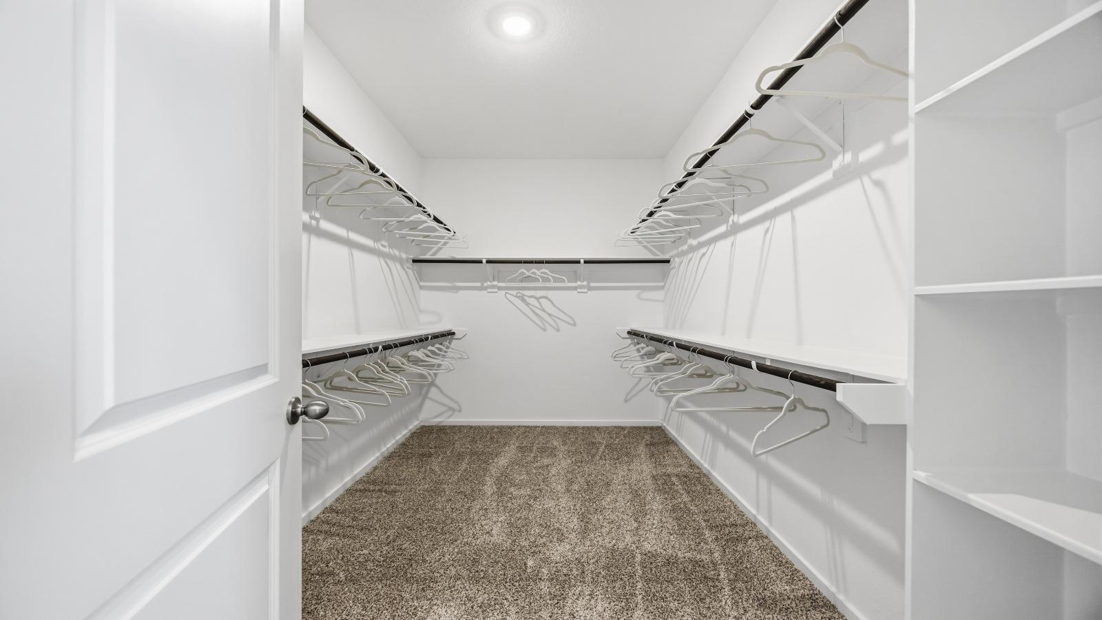 A spacious walk-in closet off the primary bathroom with multiple hanging rods, and shelves for maximum storage capabilities.