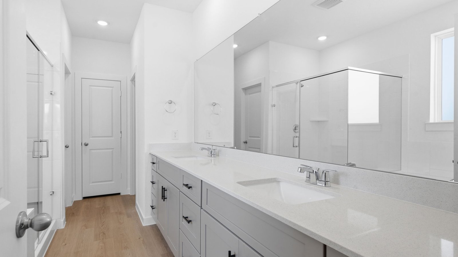 Modern primary bathroom with double vanities, granite countertops, and a glass-enclosed shower with a walk-in closet.