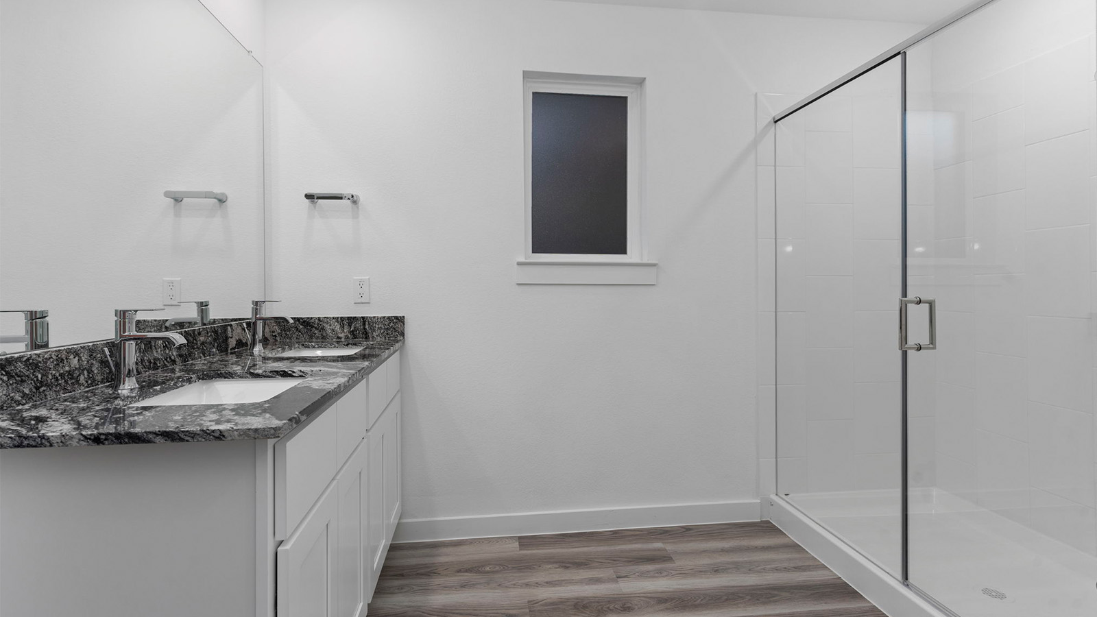 Modern primary bathroom with double vanities, granite countertops, and a glass-enclosed shower with a walk-in closet.