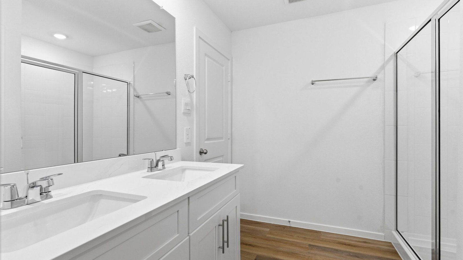 Modern primary bathroom with double vanities, granite countertops, and a glass-enclosed shower with a walk-in closet.