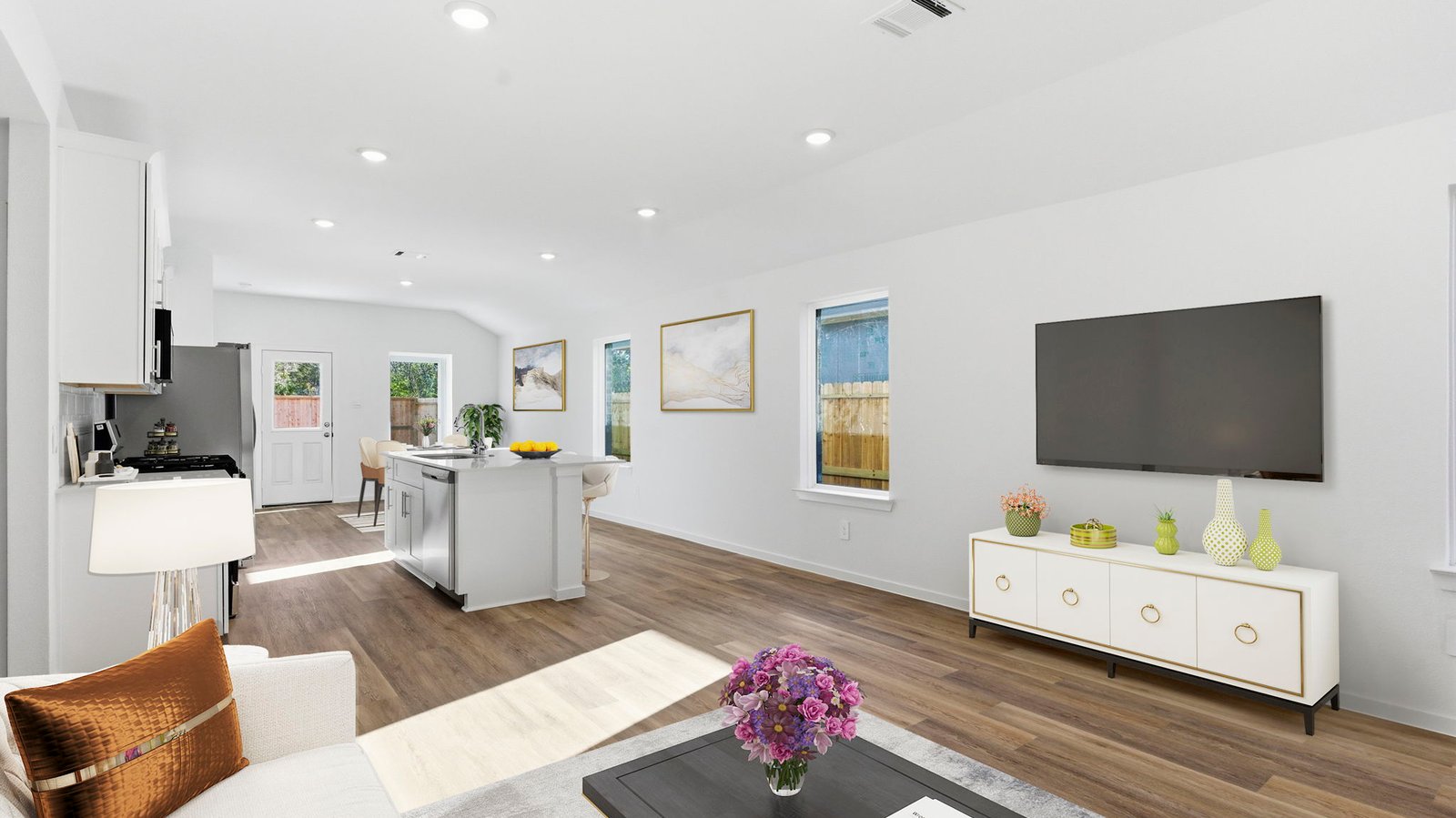 A cozy living room featuring large windows for natural lighting, vinyl wood flooring and a view to the kitchen and dining area.