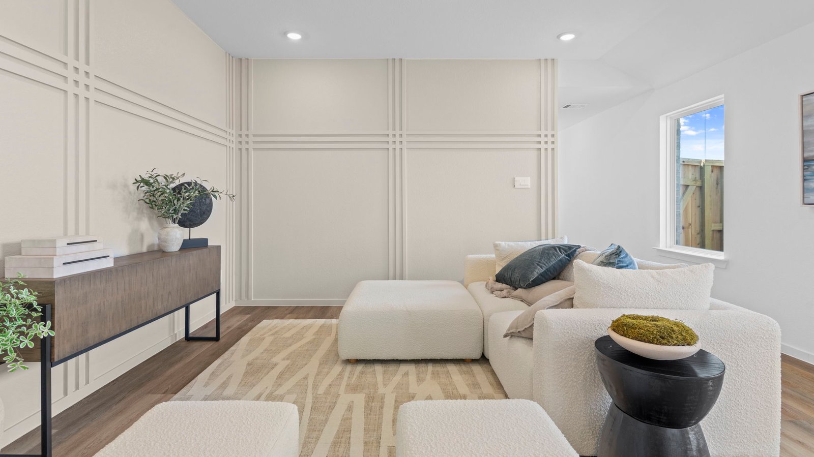A cozy living room featuring large windows for natural lighting, wood flooring and a view to the kitchen and dining ar