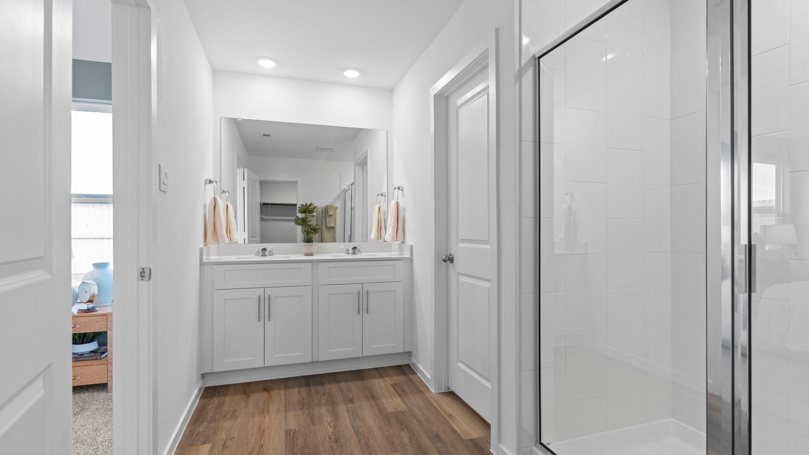 Modern primary bathroom with double vanities, quartz countertops, and a glass-enclosed shower with a walk-in closet.