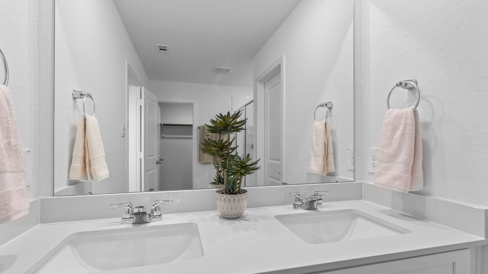 Modern primary bathroom with double vanities, quartz countertops, and a glass-enclosed shower with a walk-in closet