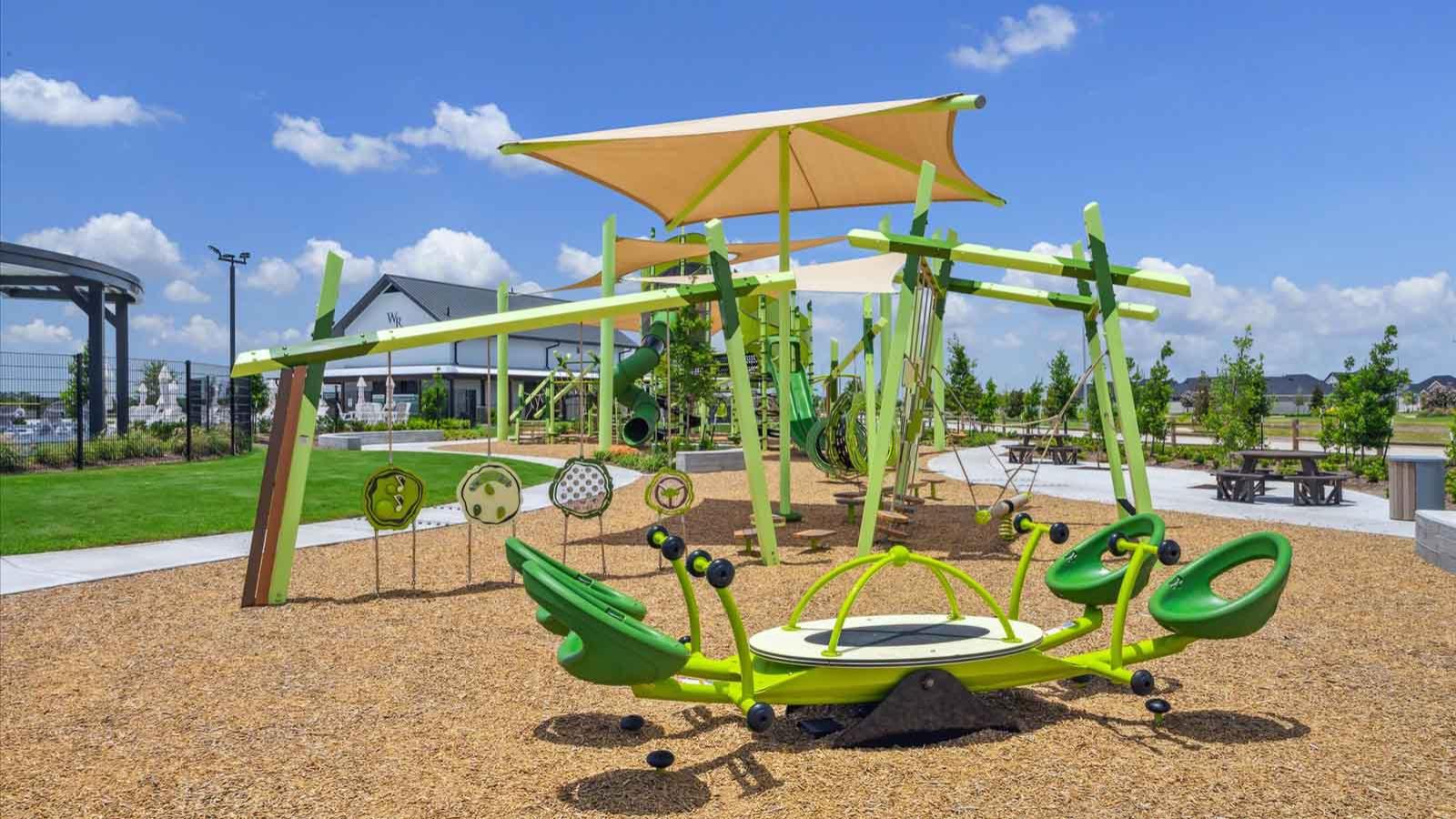 Community playground with swings, slides, and a shaded seating area surrounded by green space