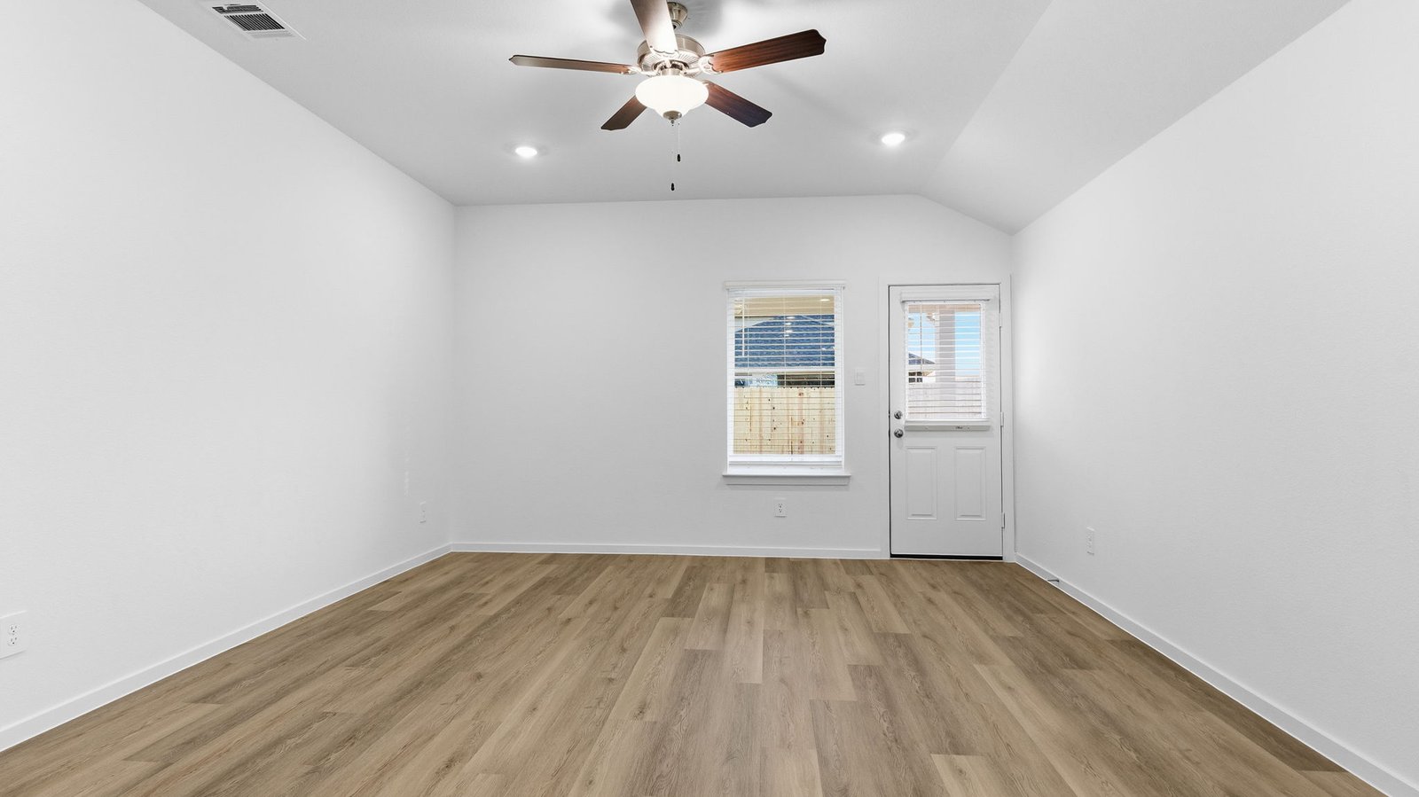 A cozy living room featuring large windows for natural lighting, vinyl wood flooring and a view to the kitchen and dining area.