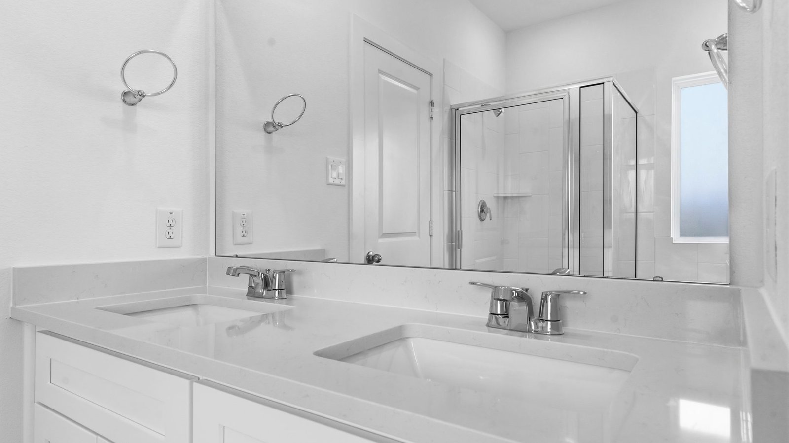 Modern primary bathroom with double vanities, quartz countertops, and a glass-enclosed shower with a walk-in closet.