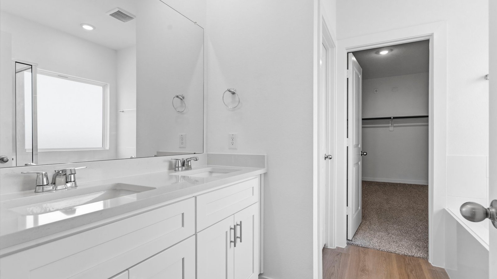 Modern primary bathroom with double vanities, quartz countertops, and a glass-enclosed shower with a walk-in closet.