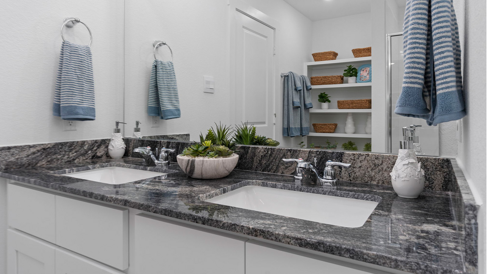 Modern primary bathroom with double vanities, quartz countertops, and a glass-enclosed shower with a walk-in closet.