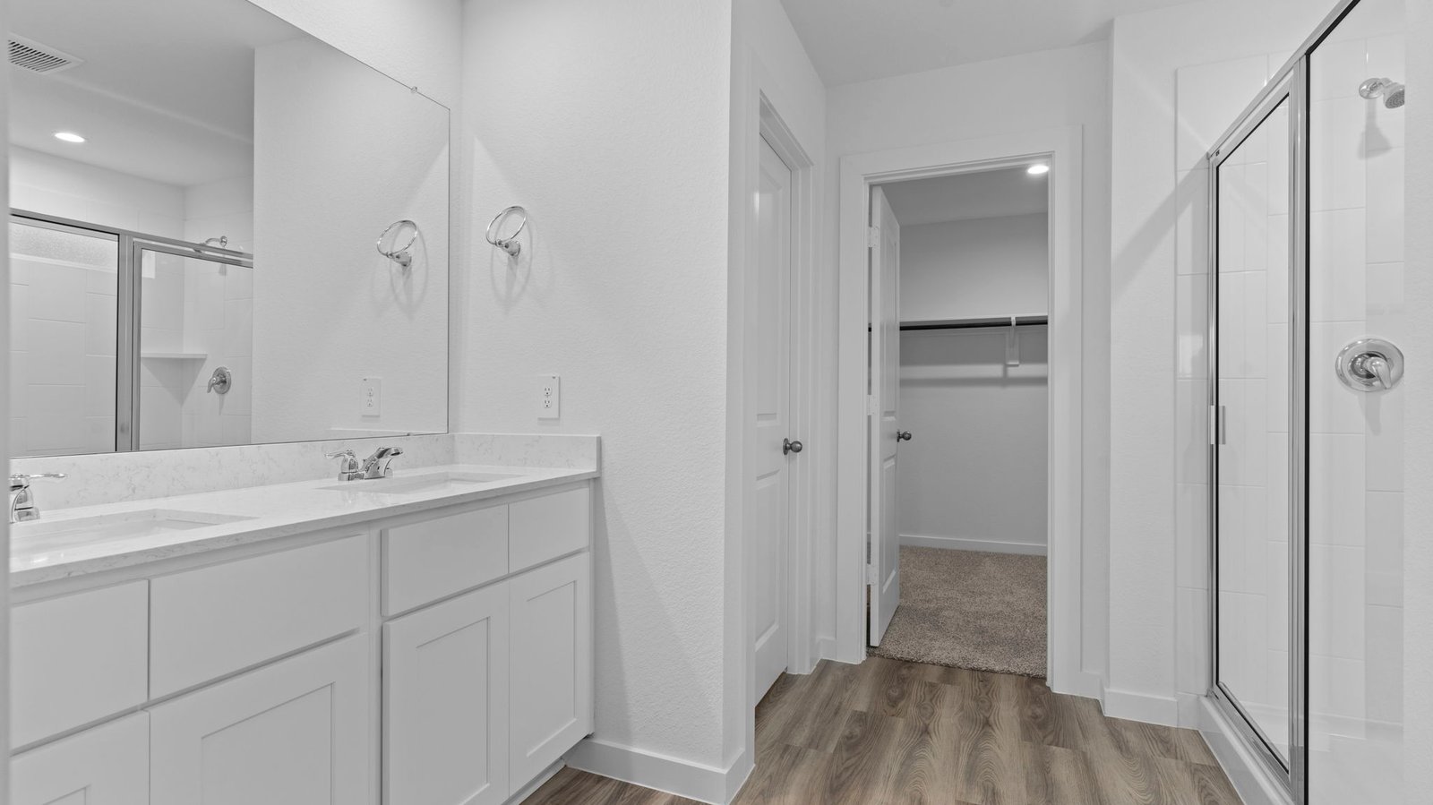 Modern primary bathroom with double vanities, quartz countertops, and a glass-enclosed shower with a walk-in closet.