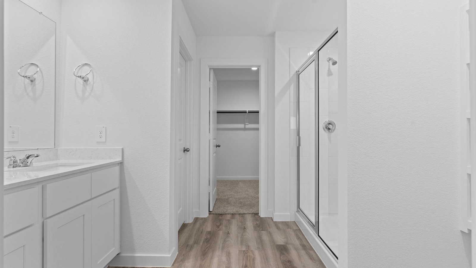 Modern primary bathroom with double vanities, quartz countertops, and a glass-enclosed shower with a walk-in closet.